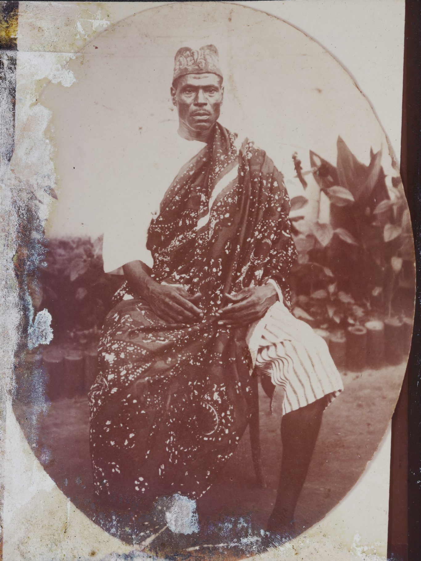 Portrait d'une personne en tenue traditionnelle, assise dans un environnement naturel.